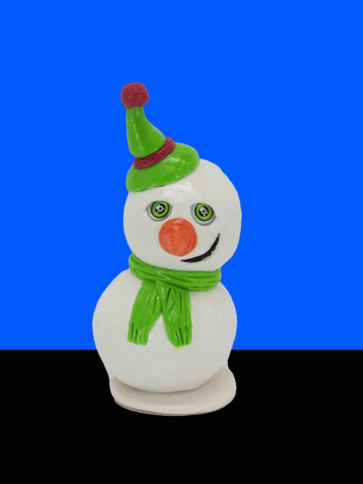 Smirky Snowman clay sculpture in front of blue and black background.